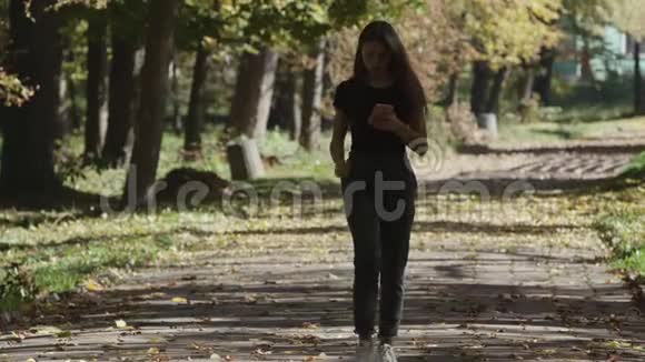 年轻女性使用智能手机在城市公园散步视频的预览图