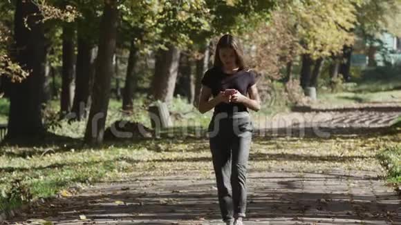 年轻女性使用智能手机在城市公园散步视频的预览图