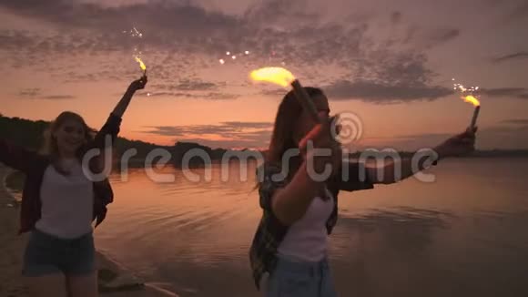 在日落时分欢乐的男女朋友正沿着海滩奔跑手里拿着闪闪发光的烟花和失控的灯光视频的预览图
