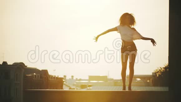 一个年轻迷人的女人卷发在建筑物的背景上表演舞蹈元素日落视频的预览图