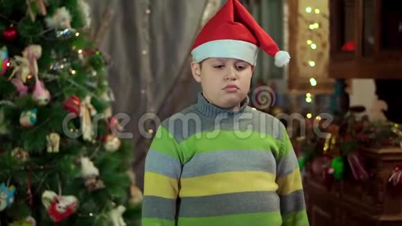 穿着圣诞老人的毛衣和帽子的男孩心烦意乱他没有天赋在这样的背景下视频的预览图