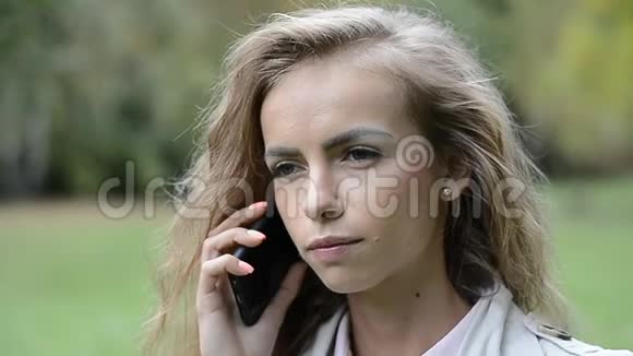 漂亮的年轻女孩用她的手机户外夏天公园里一位轻松的年轻女士在电话中交谈的肖像视频的预览图