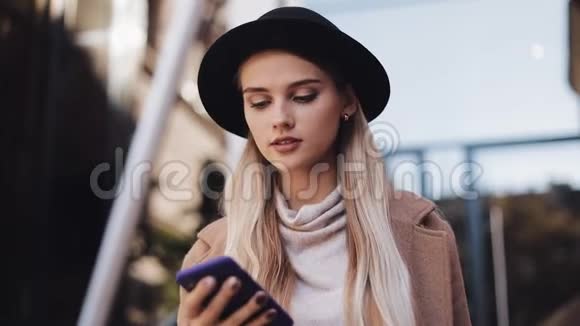 在阳光明媚的春天美丽迷人的女人穿着外套和帽子在市中心通过电话交谈视频的预览图