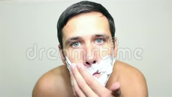 年轻的帅哥用剃须泡沫来刮胡子视频的预览图