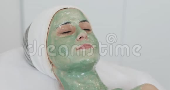水疗沙龙的女人口罩美丽的女孩躺在沙发上戴着绿色面具躺在美容诊所里视频的预览图