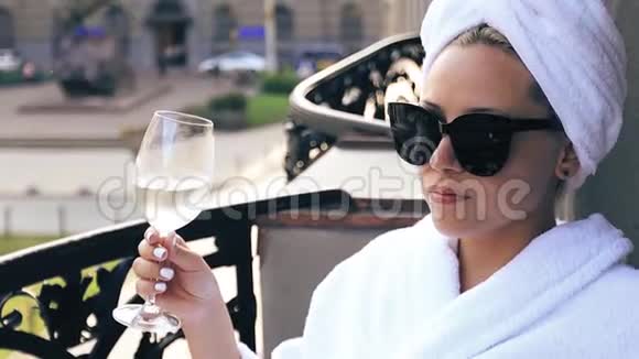 优雅的女孩穿着白色浴袍头上戴着毛巾享受着一杯白葡萄酒视频的预览图