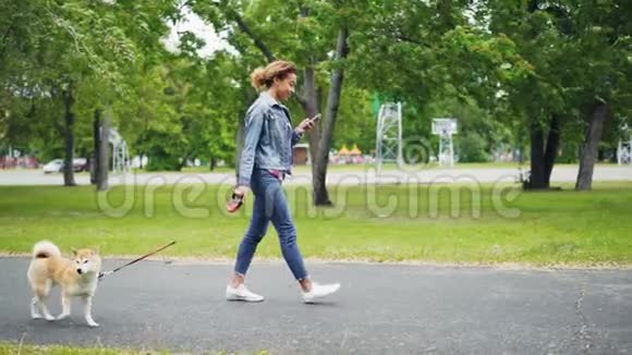 欢快的非裔美国女孩在城市公园里遛狗用智能手机慢动作视频的预览图