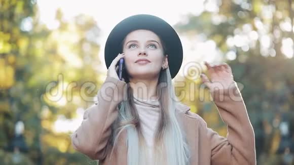 一位年轻的美女站在秋天的公园里站在一片黄叶背景下用手机说话视频的预览图