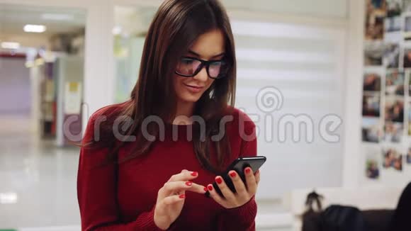 漂亮的戴眼镜的年轻女子在室内使用智能手机视频的预览图