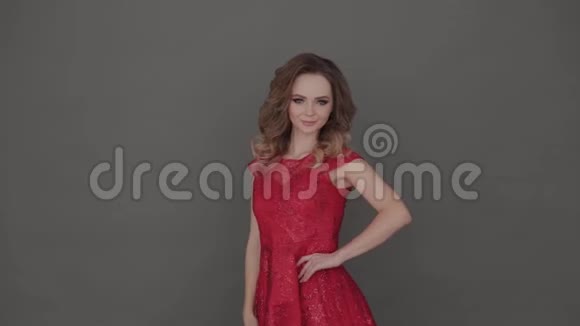 美丽的年轻女孩穿着红色的裙子在灰色的背景上摆姿势视频的预览图
