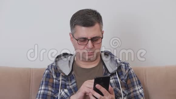 一位戴眼镜的中年男子正在智能手机上使用移动互联网而坐在房间的沙发上视频的预览图