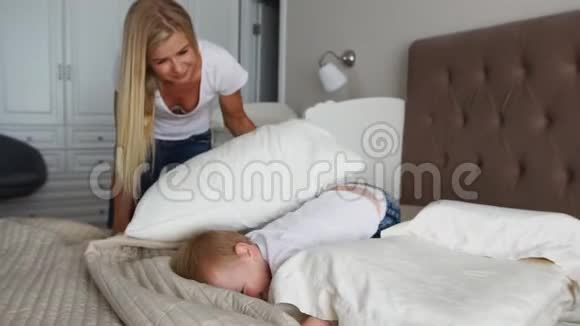年轻的母亲和父亲带着她两岁的小儿子穿着睡衣在床上放松和玩耍视频的预览图