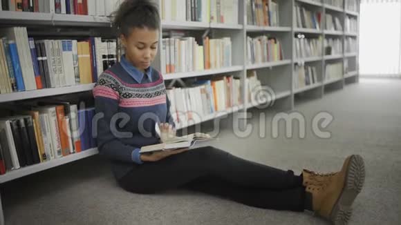 年轻的非裔美国妇女正坐在大学图书馆的地板上看书视频的预览图
