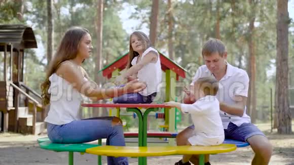 幸福的家庭概念四个家庭成员坐在一个木头公园的桌子旁在夏天交谈视频的预览图