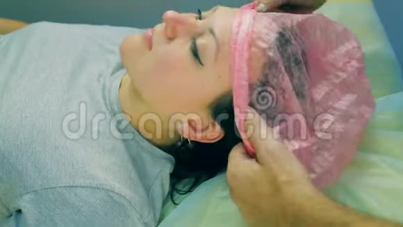 化妆师的男人的手放在一个躺在沙发上的女人的头上一顶化妆帽视频的预览图
