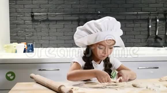 手拿擀面杖戴厨师帽的漂亮小女孩的肖像小厨师把面团和眼泪卷成碎片视频的预览图