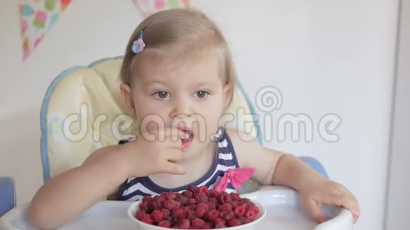 一个小女孩坐在孩子们桌子旁吃成熟的红树莓视频的预览图