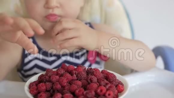 一个小女孩坐在孩子们桌子旁吃成熟的红树莓视频的预览图