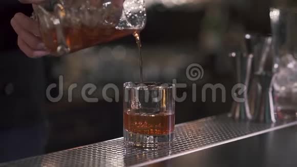 酒保把一杯清爽的威士忌或酒精鸡尾酒倒入一杯冰快关门慢动作视频的预览图