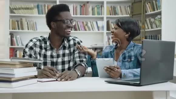 微笑非洲男女学生使用平板电脑在图书馆视频的预览图