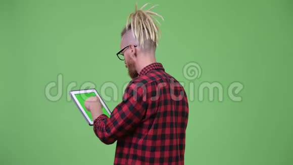 用数字平板电脑观看留着胡子的戴着可怕锁的时髦男士的背影视频的预览图