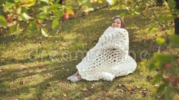 一个微笑的女孩裹着一个梅里诺格子坐在城市公园的初秋视频的预览图