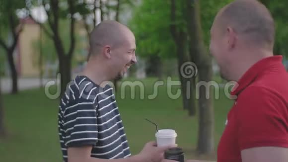 两个男人在城市公园里交流用一次性塑料眼镜喝咖啡视频的预览图