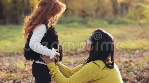 快乐的年轻母亲和她的小红发女儿在秋天的公园里玩得很开心他们玩接吻拥抱视频的预览图