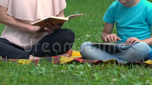 妈妈在公园看书儿子在平板电脑上打字玩得很开心视频的预览图