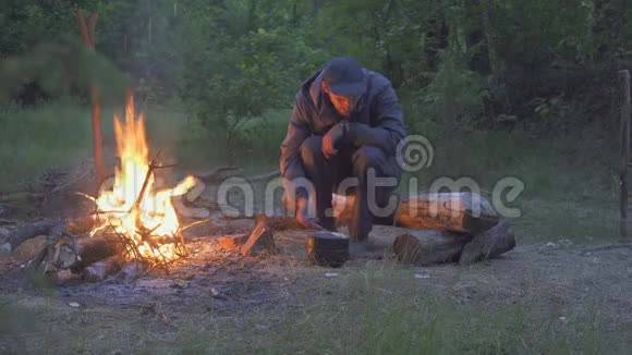 晚上男性旅行者从火旁的锅中进食视频的预览图