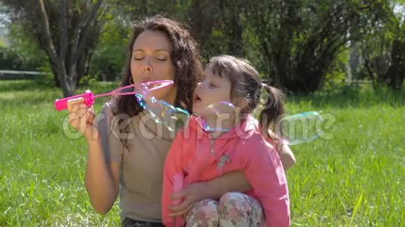 一个和她母亲在一起的孩子在玩肥皂泡野外的幸福家庭妈妈和女儿在吹泡泡视频的预览图