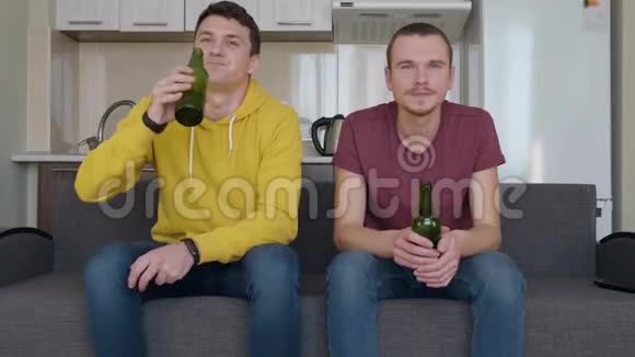两个人坐在沙发上看电视上的足球赛喝啤酒视频的预览图