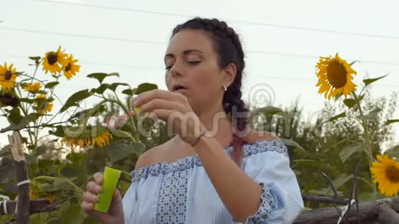慢动作特写美丽的村妇带着硬币让肥皂泡在成长中的向日葵背景上视频的预览图