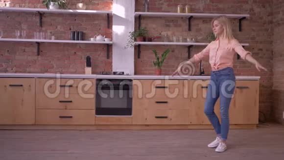 快乐的运动女孩在家里的厨房里做体操动作视频的预览图
