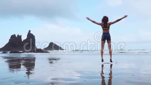 女孩在大西洋附近的黑沙滩上跳汉堡包背景是群山视频的预览图