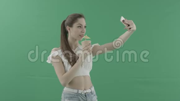 迷人的年轻女性在绿色背景下用鸡尾酒自拍视频的预览图