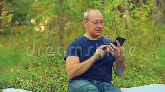森林里一个戴眼镜的人坐在草地上在平板电脑上用信使传达信息视频的预览图