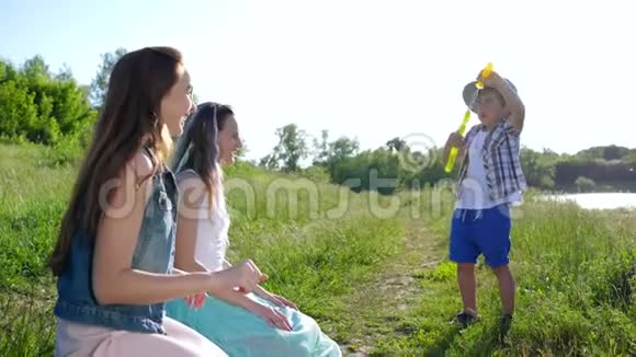 快乐的孩子生活戴帽子的好男孩吹肥皂泡在坐在草地上的少女身上视频的预览图