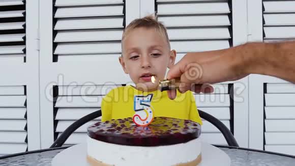 小男孩坐在桌边吹生日蛋糕上的蜡烛可爱的快乐男孩庆祝它的五岁生日在视频的预览图