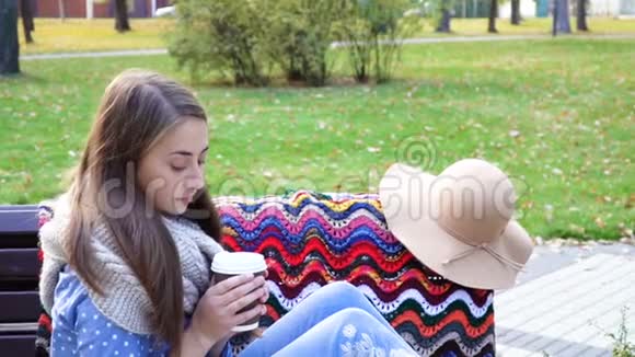 女人在美丽的绿色公园的长凳上放松喝杯咖啡视频动作漂亮的女孩坐在木头上视频的预览图