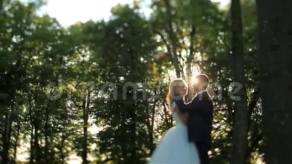 可爱的新婚夫妇在森林里轻轻地接吻背景上美丽的日落迷人的时刻视频的预览图