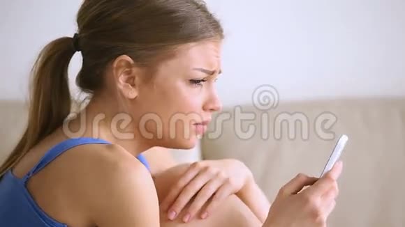 少女在沙发上哭泣拿着智能手机被信息弄得心烦意乱视频的预览图