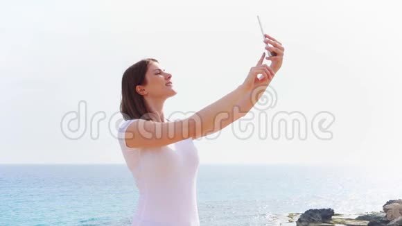 微笑的年轻女子在手机上慢镜头拍摄自拍照片视频的预览图