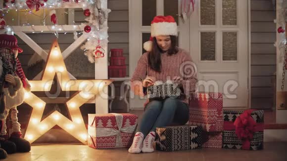 戴着圣诞帽的漂亮女孩正坐在门廊里包装圣诞礼物视频的预览图