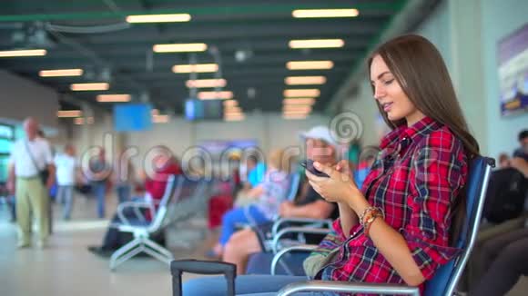 在机场用智能手机的女人旅行者女孩在机场等着用她的智能手机年轻漂亮的女性视频的预览图