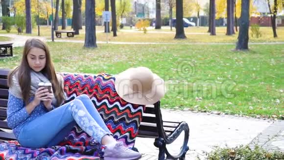 女人在美丽的绿色公园的长凳上放松喝杯咖啡视频动作漂亮的女孩坐在木头上视频的预览图