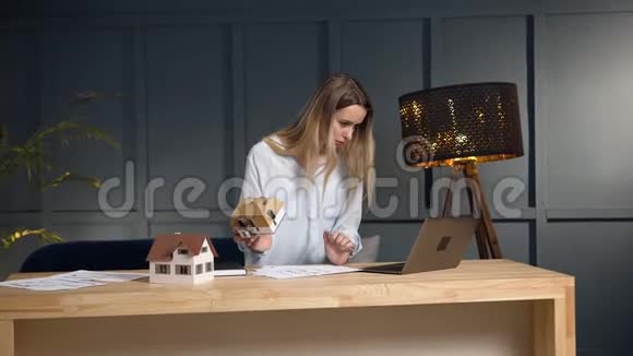 年轻建筑师使用笔记本电脑与蓝图和房屋模型工作视频的预览图