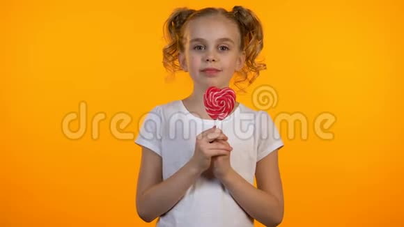 漂亮的糖果女孩舔着美味的心形棒棒糖微笑着快乐着视频的预览图