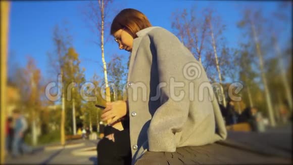 穿外套的女孩在阳光明媚的天气里坐在公园里笑着戴上眼镜视频的预览图