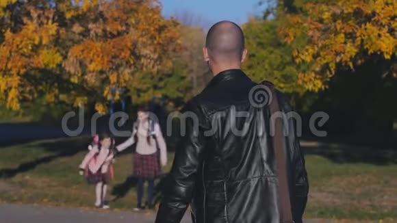 年轻快乐的父亲从学校遇到他的女儿两个和爸爸穿校服的女孩秋天的日落视频的预览图